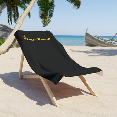 Black beach towel with 'King of the Beach' logo on a wooden chair at a tropical beach.
