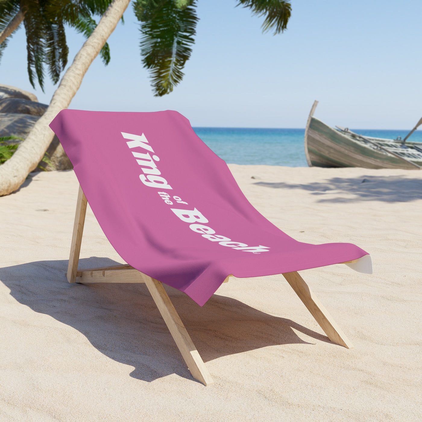 Pink towel with 'King of the Beach' text on a beach chair by the ocean.