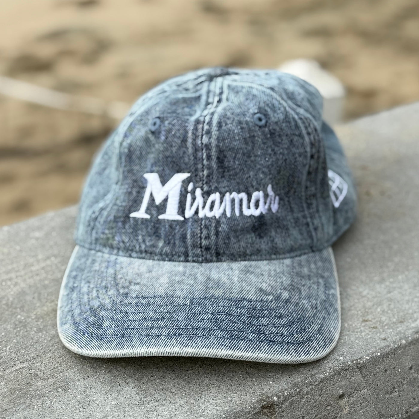 blue cap with 'Miramar' logo on a stone surface with a blurred natural background